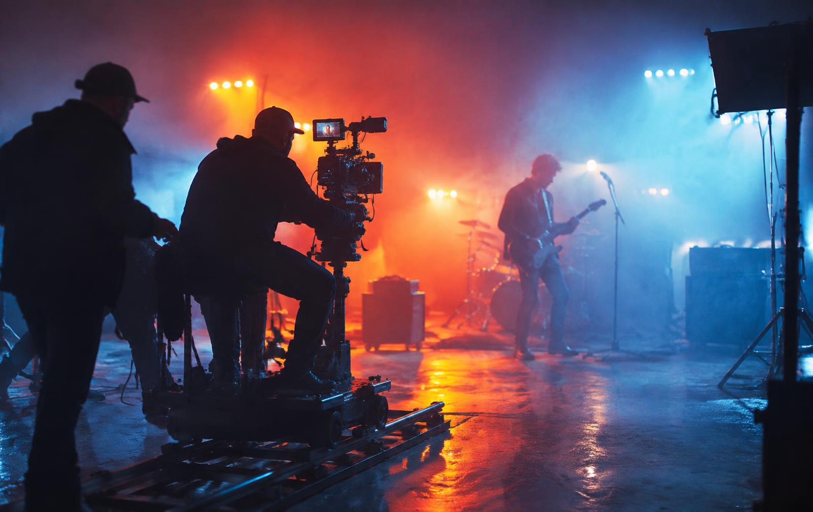 Film crew with cinema camera shooting a music video on a smoky lit stage